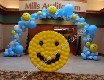 Photo of blue and yellow baloon arch behind a yellow smiley face